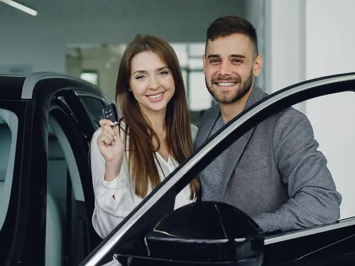 A couple beside an open car door holding the keys to their new car