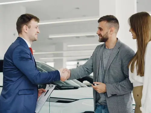 A salesperson shaking hands with two customers in the JE Auto showroom